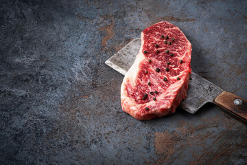 Wall Mural - Juicy Raw new York beef steak and a butcher's hatchet close up on a dark background, copy space