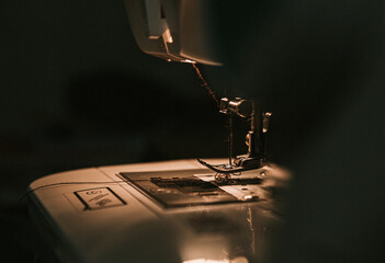 Old sewing machine with black thread scissors and needle, on a old grungy work table. Tailor's work table. textile or fine cloth making. industrial fabric