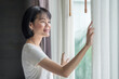 © Thannaree - Asian woman smile and looking at outdoor with curtain at a room in the hotel