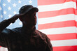 patriotic military man in uniform and cap giving salute near american flag on background