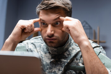 Wall Mural - tired military man in uniform looking at laptop on blurred foreground