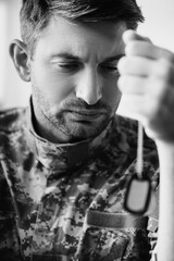 Wall Mural - sad soldier in camouflage uniform holding military tag, monochrome