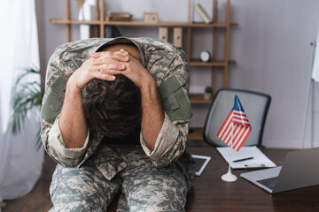 Wall Mural - military man sitting on desk and leaning near gadgets and american flag