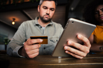 Close up of stressed man and female in coffee shop about to make an online payment with credit card, holding digital tablet