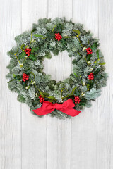 Wall Mural - Christmas holly, mistletoe & snow covered spruce fi winter wreath with red bow on rustic wood front door background. Traditional theme for the solstice, xmas & New Year. Copy space.