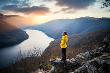 woman on rock enjoying amazing autumn view over lake at sunset