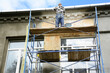 © bildlove - A building contractor standing on scaffolding is rendering, applying a stucco layer, plastering the facade, exterior wall of a building.