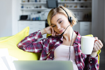 Wall Mural - young blonde woman in headphones working from home and drinking tea