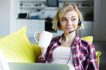 young blonde woman in headphones working from home and drinking tea