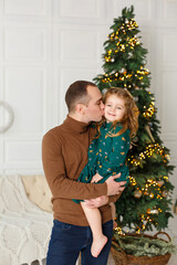 Wall Mural - Little girl with her father near fir-tree. Christmas celebration. Girl with Dad weared in green and brown clothes. New year eve