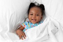 Happy Baby Girl With Hair Buns Lying On White Bed