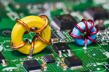 Two toroid inductors and electronic transistors on green circuit board. Beautiful yellow or blue induction coil on PCB in embedded voltage converter of computer mainboard detail. Semiconductors. Tech.