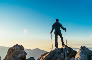 Wall Mural - young hiker man standing with trekking poles on a cliff edge and looking at tatra mountains valley c