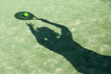 Shadow of a girl playing padel, tennis with a yellow ball on the green grass.