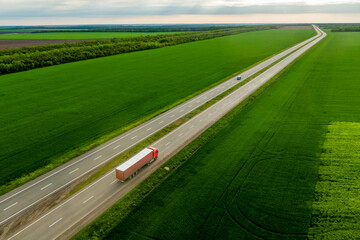 Wall Mural - red truck driving on asphalt road along the green fields. seen from the air. Aerial view landscape. drone photography.  cargo delivery