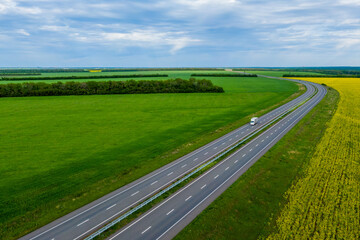 Wall Mural - cargo delivery white truck driving on asphalt road along the green fields. seen from the air. Aerial view landscape. drone photography.