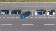 TOP DOWN: Flying above a shiny blue car driving out of a roadside parking space.