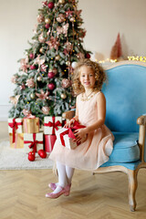 Wall Mural - Little girl near fir-tree with Christmas gifts. Christmas celebration. Child Girl weared in white blouse and high black boots holding a New Year's gift in her hands. New year eve