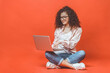 © denis_vermenko - Happy young curly beautiful woman sitting on the floor with crossed legs and using laptop on red background.