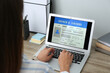 © New Africa - Woman using laptop to fill driver's license application form at table in office, closeup