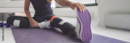 Home workout woman stretching legs on exercise mat before training. Closeup of running shoe banner panoramic. Purple shoes and floor cover.