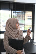 © Prathankarnpap - Portrait of cheerful muslim young woman in abaya hand holding document file and pen while standing in office.
