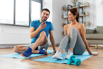 Wall Mural - fitness, sport and technology concept - happy couple with smartphone doing sports at home