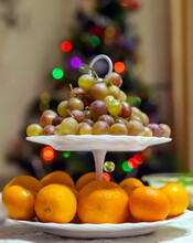 Grapes And Tangerines On A Two-tier White Plate Close-up Against A Christmas Tree