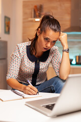 Concentrated freelance woman working overtime to finish a project from home kitchen. Employee using modern technology at midnight doing overtime for job, business, career, network, lifestyle ,wireless