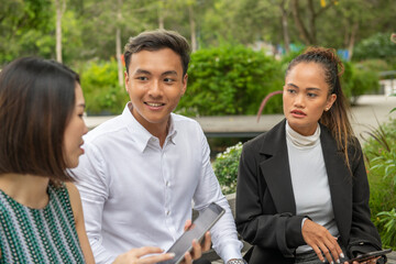 Canvas Print - Outdoor business meeting. One asian man and two asian women discussing business details seated on a public bench