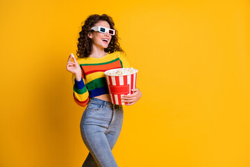 Poster - Photo of cheerful funky young brunette hair lady stand eat popcorn watch film wear spectacles sweater jeans isolated on yellow background