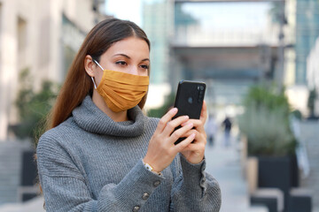 Wall Mural - Portrait of young woman standing on street in protective mask and messaging with smartphone