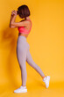 © Анастасия Каргаполов - Sport and yoga lifestyle concept. Young fit pretty strong woman dressed in sport clothes, stylish top and leggings, poses against yellow background. Studio shot.