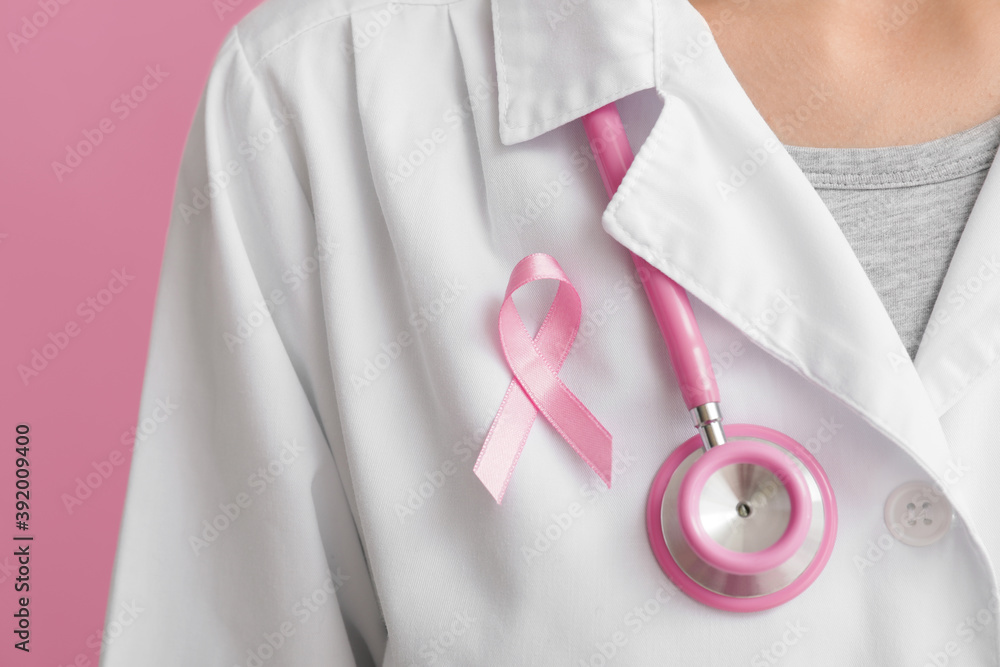Doctor with pink ribbon on color background, closeup. Breast cancer awareness concept
