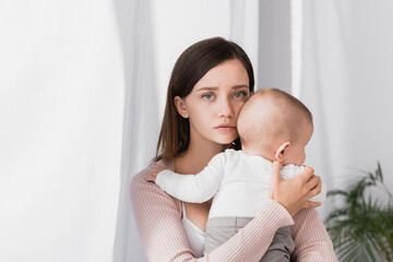 worried mother holding in arms baby boy and looking at camera