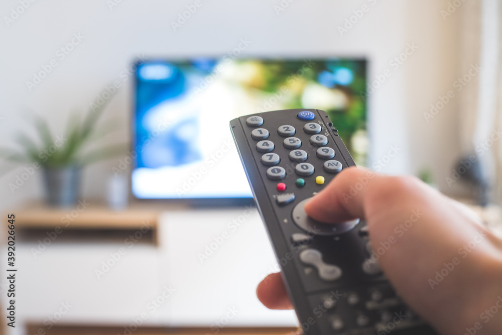 Male hand is holding TV remote control, streaming on a smart TV. - obrazy, fototapety, plakaty 