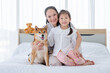© narong - Asian mother and girl sit on white bed with Shiba dog and look to camera with smiling in bedroom. Concept of happy family feel relax to stay home with their own pets.