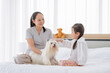 © narong - Little Asian girl play with white dog and sit near her mother to take care in bed room. Concept of happy family feel relax to stay home with their own pets.