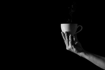 A woman holding a white ceramic tea cup in the dark.