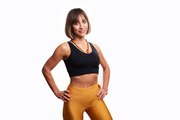 Beautiful woman posing smiling in front of white background with yoga leggings and black sports tank top. Athletic woman posing smiling against a white background, showing off her muscles.