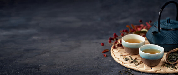 Wall Mural - Green Tea Composition with blue teapot on dark background banner. Chinese traditional tea set, ceremony concept, selective focus, copy space.