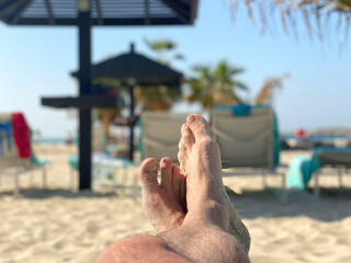 Canvas Print - Holiday concept. male feet close-up relaxing on beach, enjoying sun and splendid view