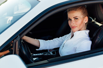 beautiful female blonde driver behind the wheel of a white car