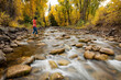 © Cavan Images - Woman crossing stream in forest during autumn