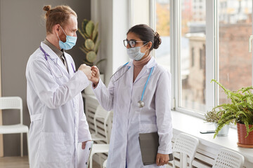 Wall Mural - Two medical colleagues in masks greeting each other standing at the corridor