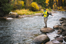 Man Fly Fishing While Standing On Rock At Roaring Fork River During Autumn