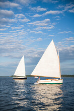 Two Catboat Sailboats Sailing During Golden Hour Sunset In Summer