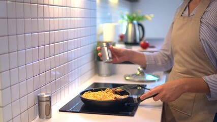 Wall Mural - Cooking woman housewife wearing apron preparing food in a frying pan on the stove for dinner at modern loft style kitchen