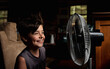© Cavan Images - Young boy smiling as he is cooling off in front of a fan in dark room.