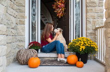 Woman And Her Dog Sitting In Doorway Of Home Decorated For Fall.